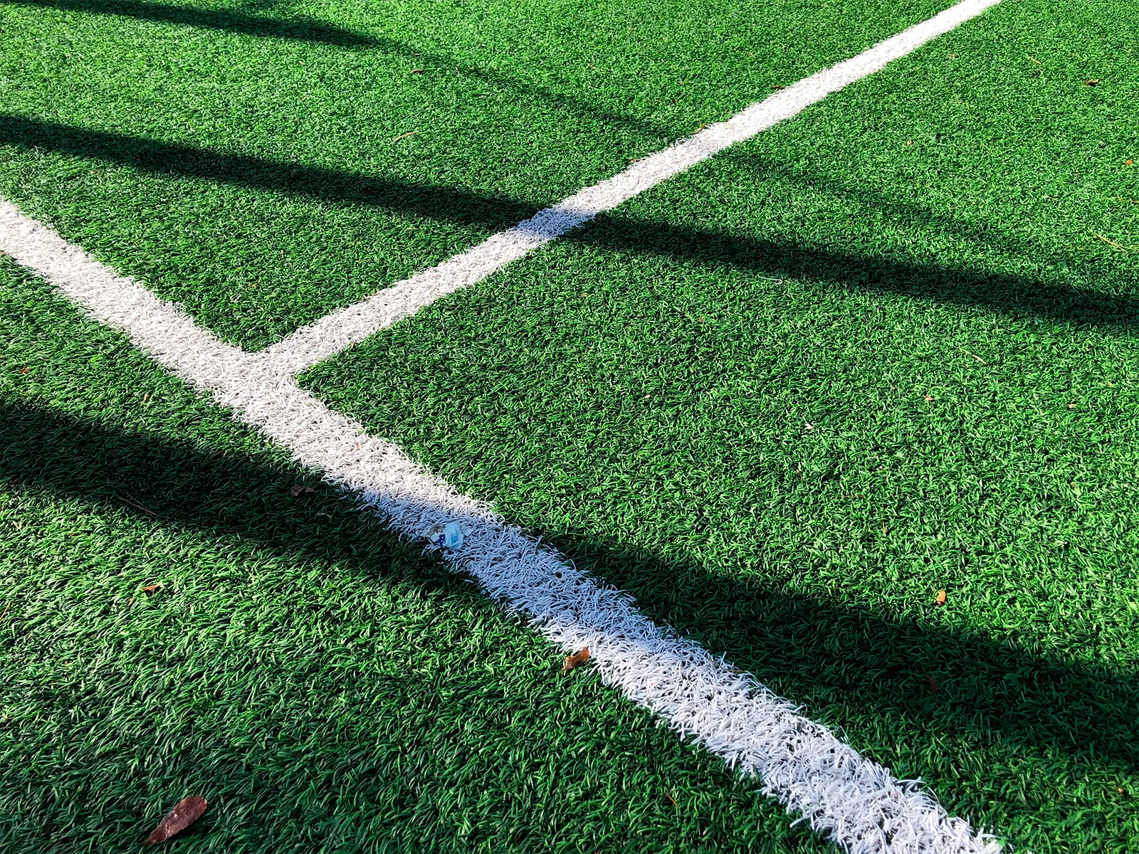 Lo zoom su un campo di calcio in erba, in particolare sul dettaglio dell'intersezione di due linee bianche del campo di gioco.